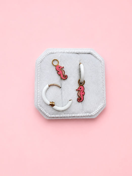 Jewelry set with seahorse charms on a white hoop on a jewelry box against a pink background