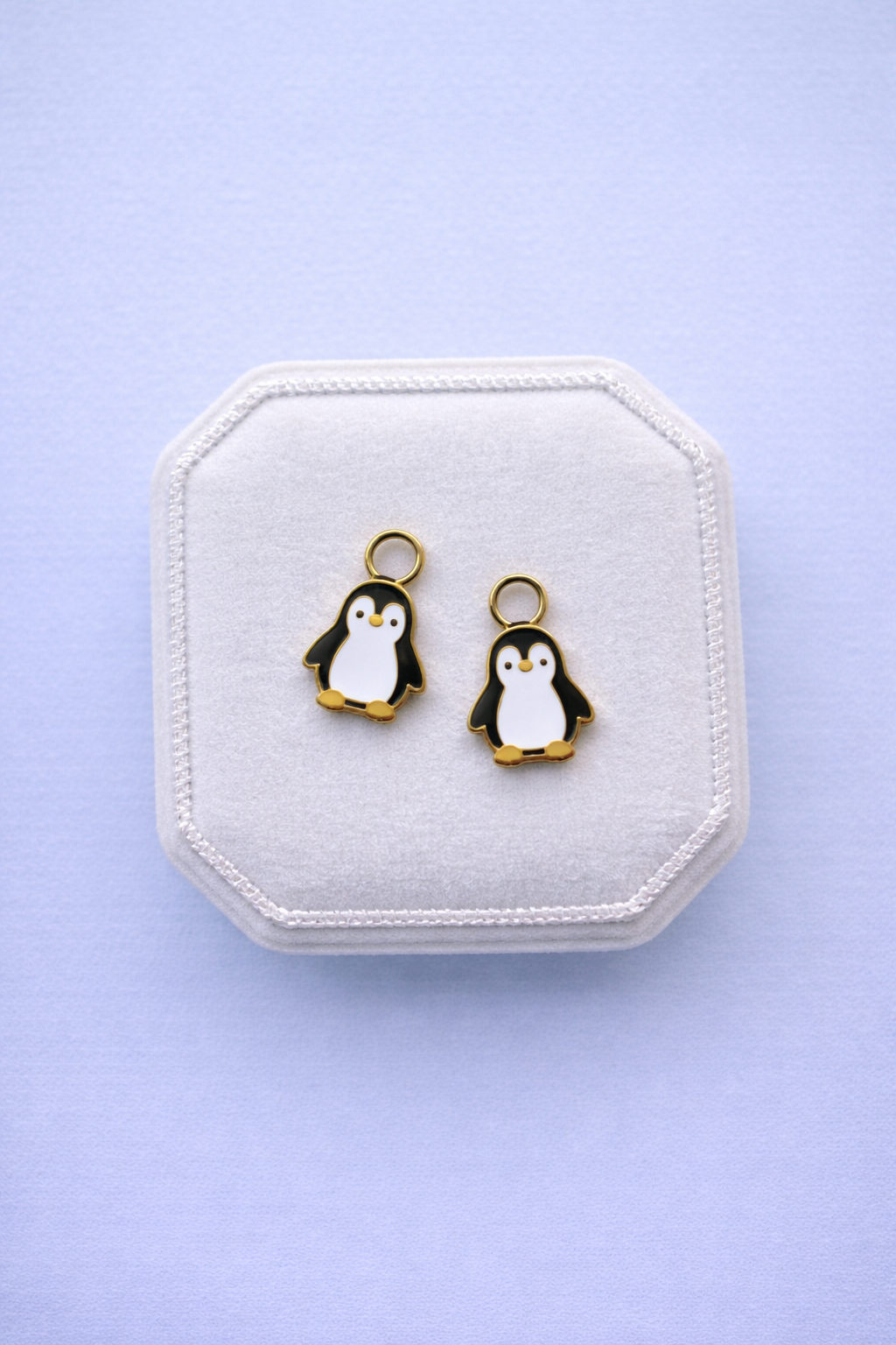 Penguin-shaped earrings on a white jewelry box with a light purple background