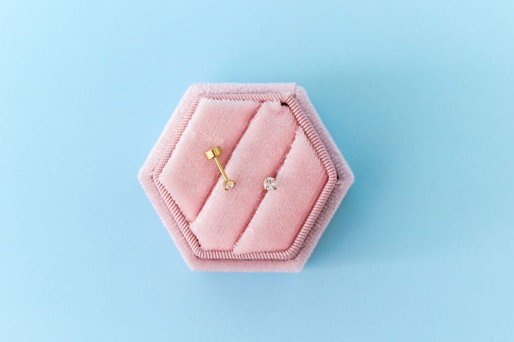 Pink hexagonal jewelry box with gold earrings on a light blue background