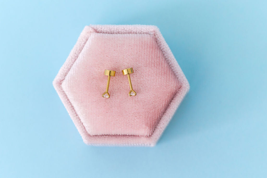 Gold earrings on a pink hexagonal jewelry box against a light blue background