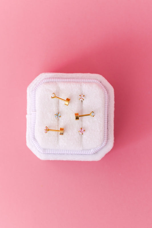 Set of gold earrings on a white cushion with a pink background