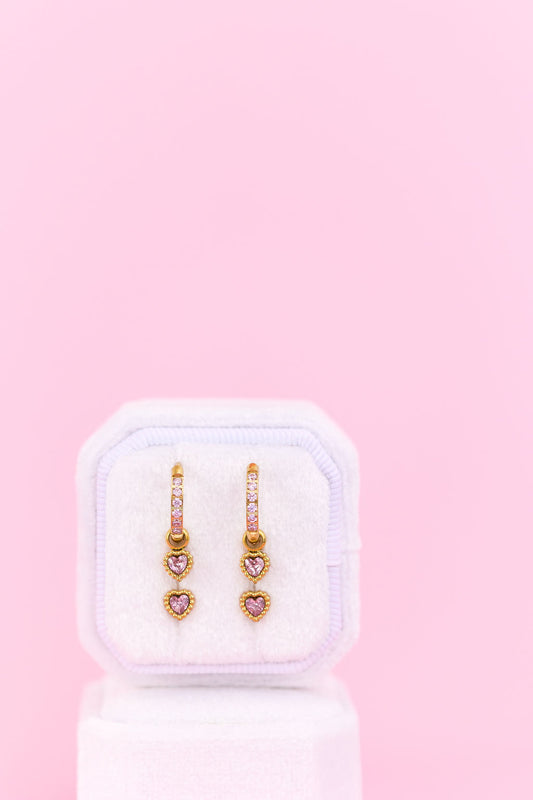 Heart-shaped earrings in a white box on a pink background