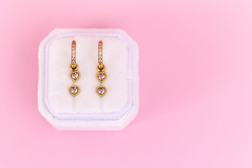 Pair of heart-shaped earrings on a white jewelry pouch against a pink background