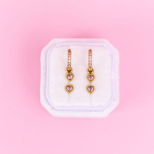 Heart-shaped earrings in a white box on a pink background