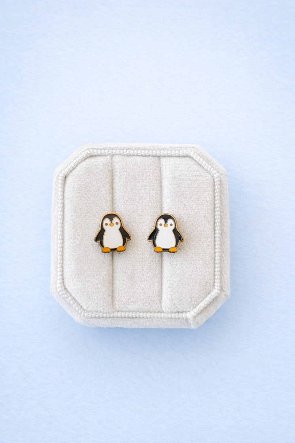 Penguin earrings on a textured white stand against a light blue background