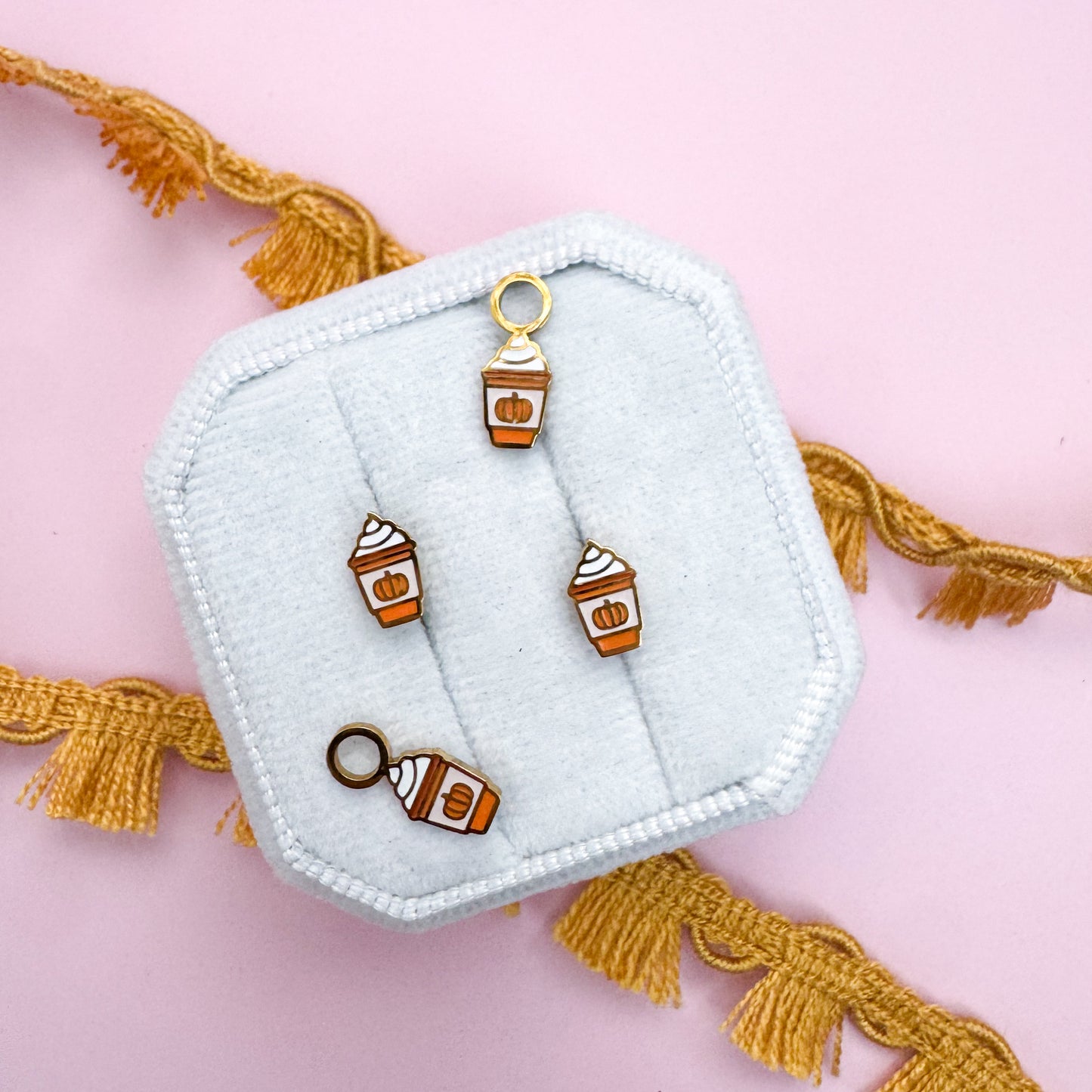 Set of pumpkin spice latte coffee-themed charms on a light blue hexagonal stand with tassels on a pink background