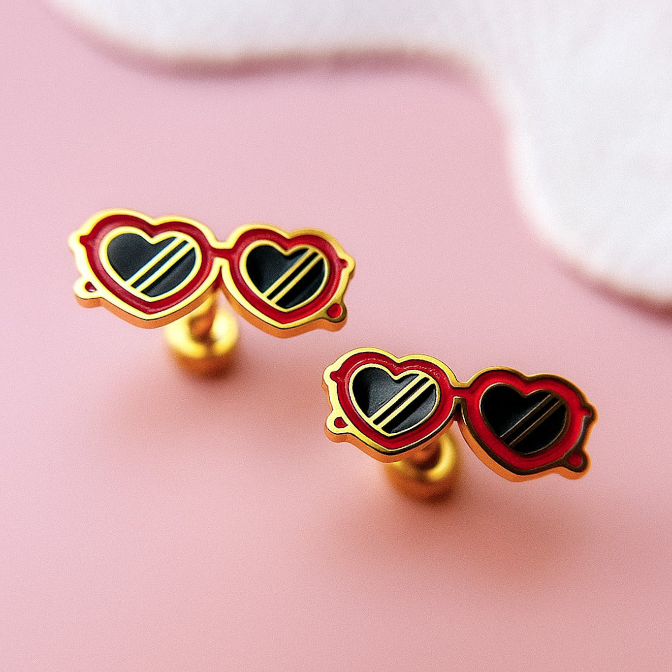 Heart-shaped sunglasses earrings on a pink background