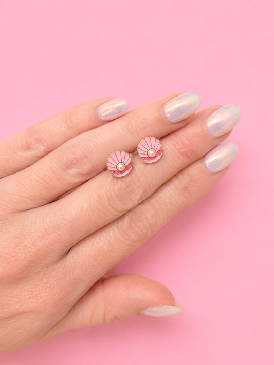 Hand holding two pink seashell-shaped earrings with pearl detail against a pink background