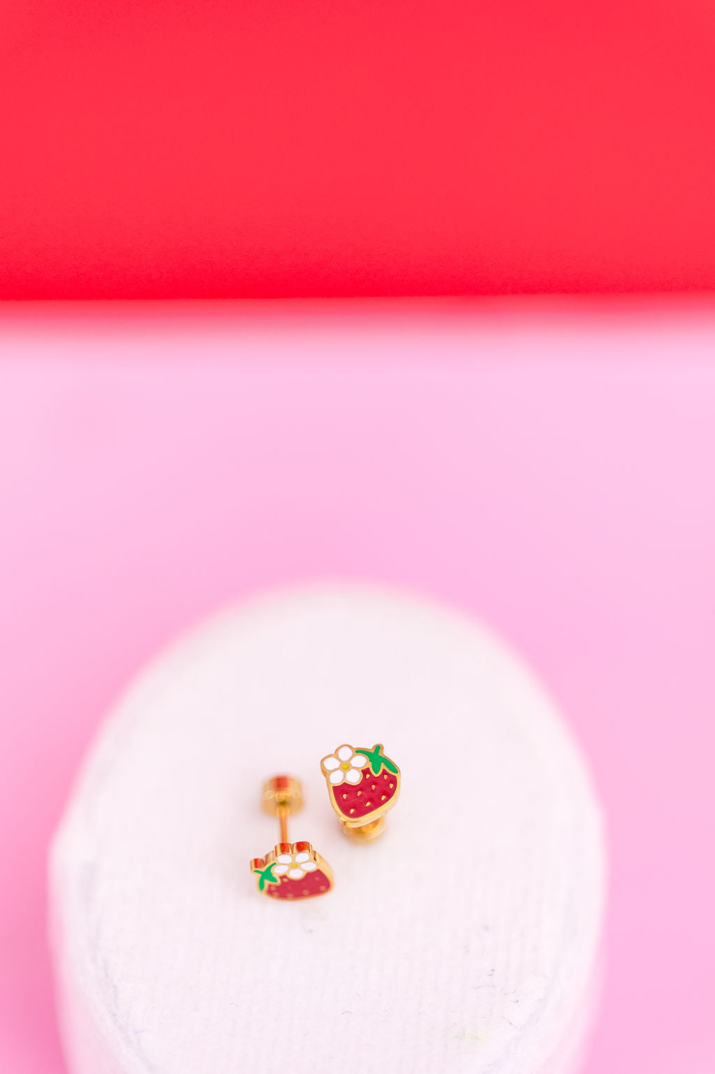 Pair of strawberry-themed earrings on a pink background