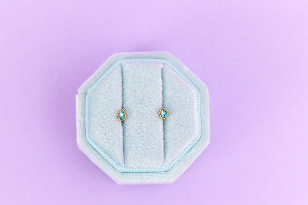 Pair of earrings in a hexagonal blue holder on a light purple background