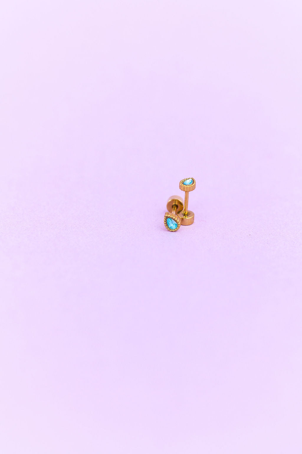 Gold earring with turquoise gemstones on a light purple background
