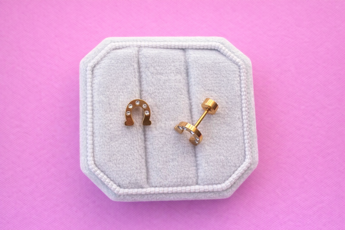 Horseshoe-shaped earrings with rhinestones and flat backs on a white cushion against a pink background