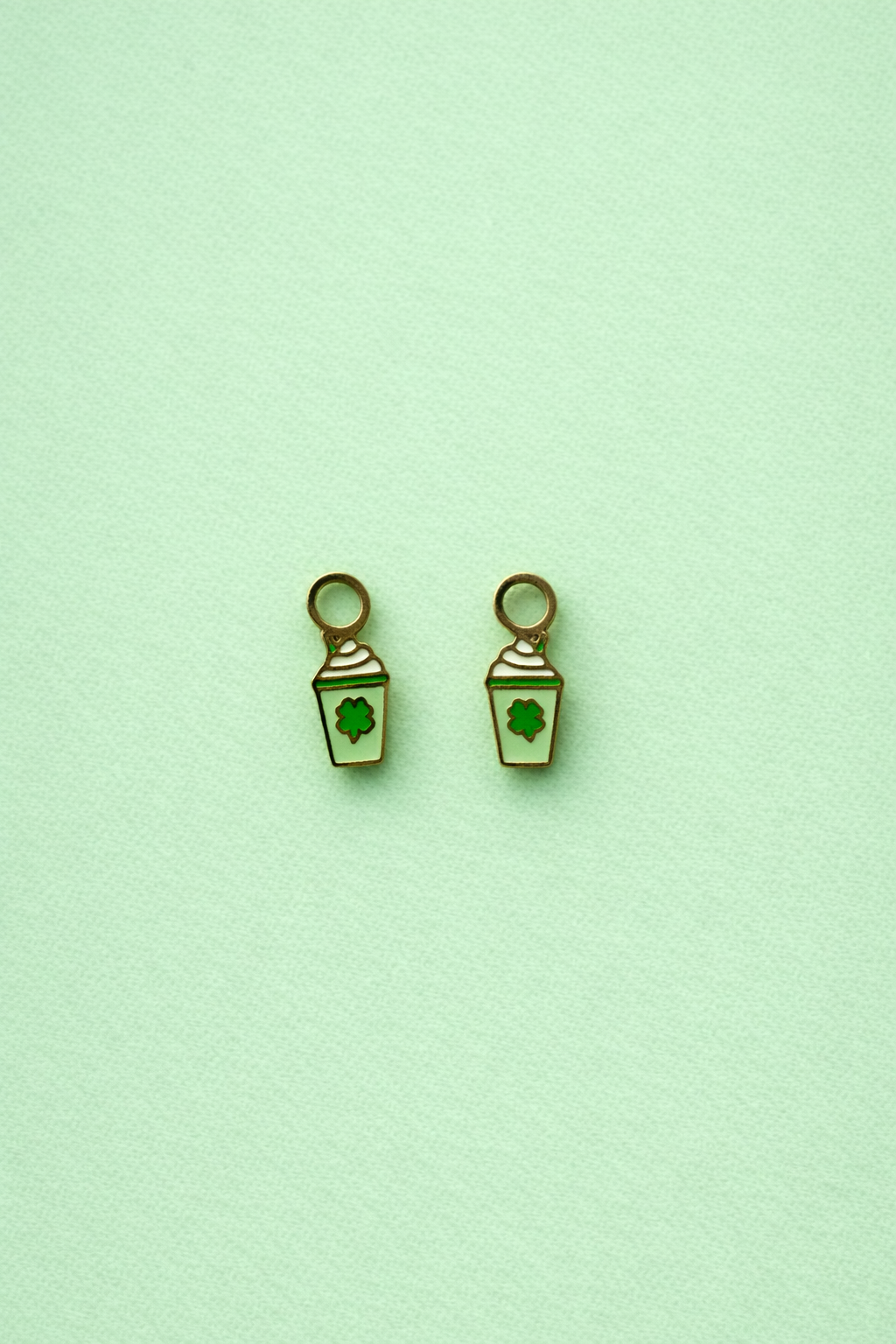Pair of green milkshake-shaped charms against a light green background