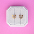 Horseshoe-shaped earrings with rhinestones on a white cushion against a pink background