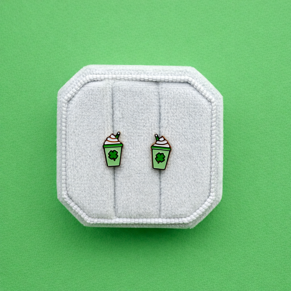 Milkshake-shaped earrings on a white cushion against a green background