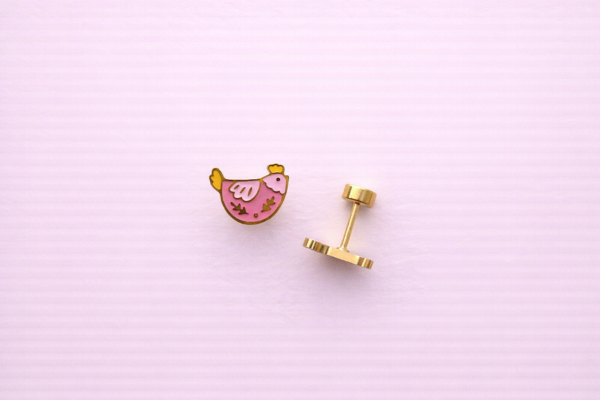 Pair of pink and yellow chicken-shaped earrings propped up and sideways on a light pink background