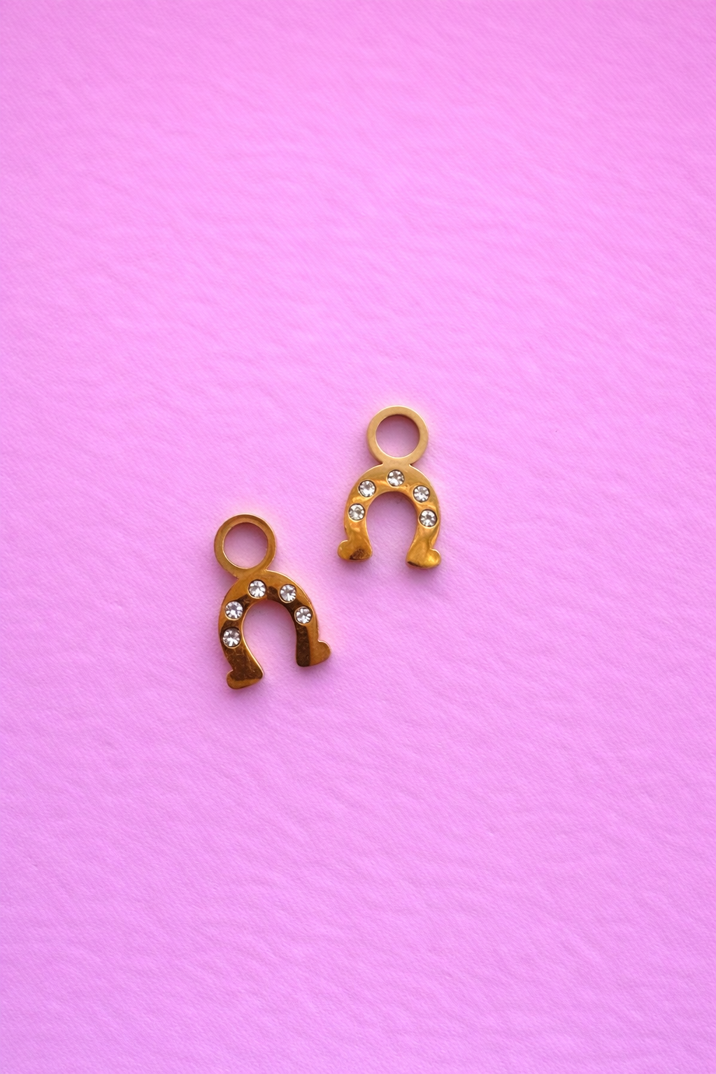 Two gold horseshoe charms with cz accents against a pink background