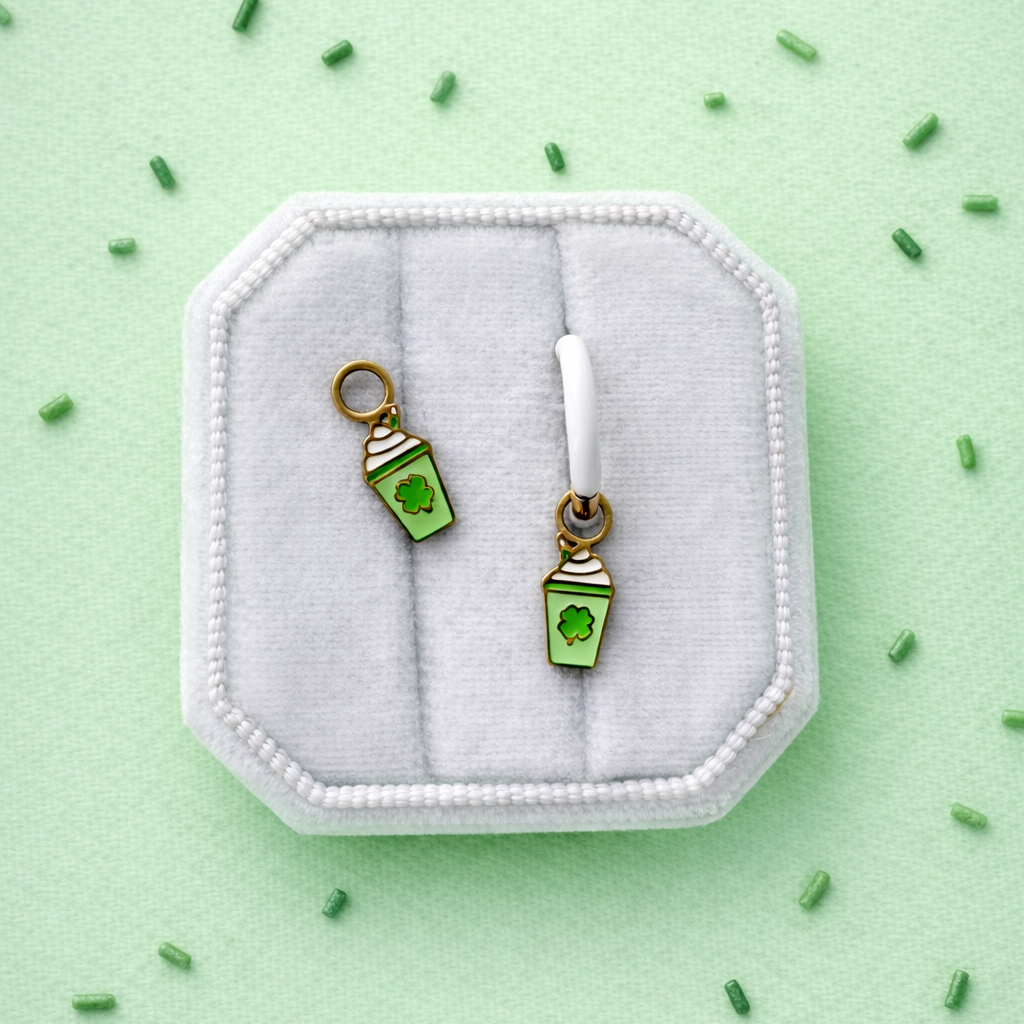 Pair of green milkshake-shaped earrings on a white cushion against a light green background with small green sprinkles