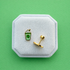 Milkshake-shaped earrings with flat backs on a white cushion against a green background