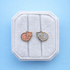 Tabby cat themed screw on flat back earrings with an orange cat and a light blue cat on a white jewelry box cushion against a light blue background