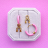 Two light pink huggie hoops with horseshoe charms with cz accents on a white jewerly box against a pink background