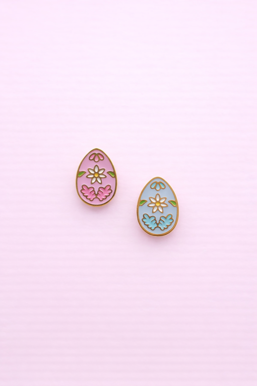 A set of floral egg stud earrings 1 pink and 1 light blue against a light pink background