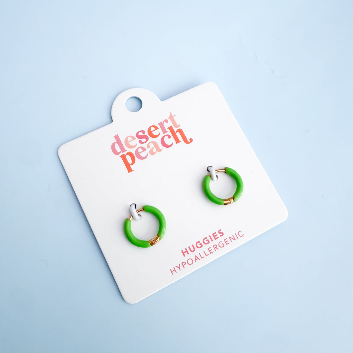 Bright green hoop earrings on a 'desert peach' branded card against a light blue background