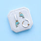 Jewelry set with dolphin-themed earrings on a hexagonal white stand against a light blue background