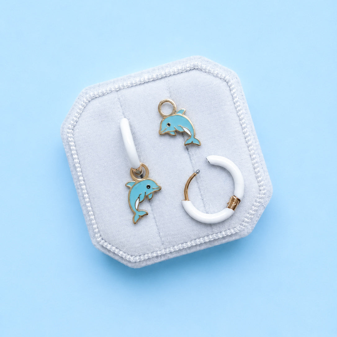 Jewelry set with dolphin-themed earrings on a hexagonal white stand against a light blue background
