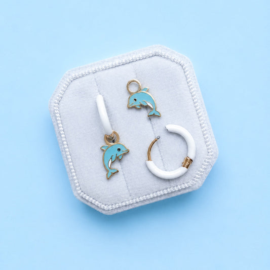 Jewelry set with dolphin-themed earrings on a hexagonal white stand against a light blue background
