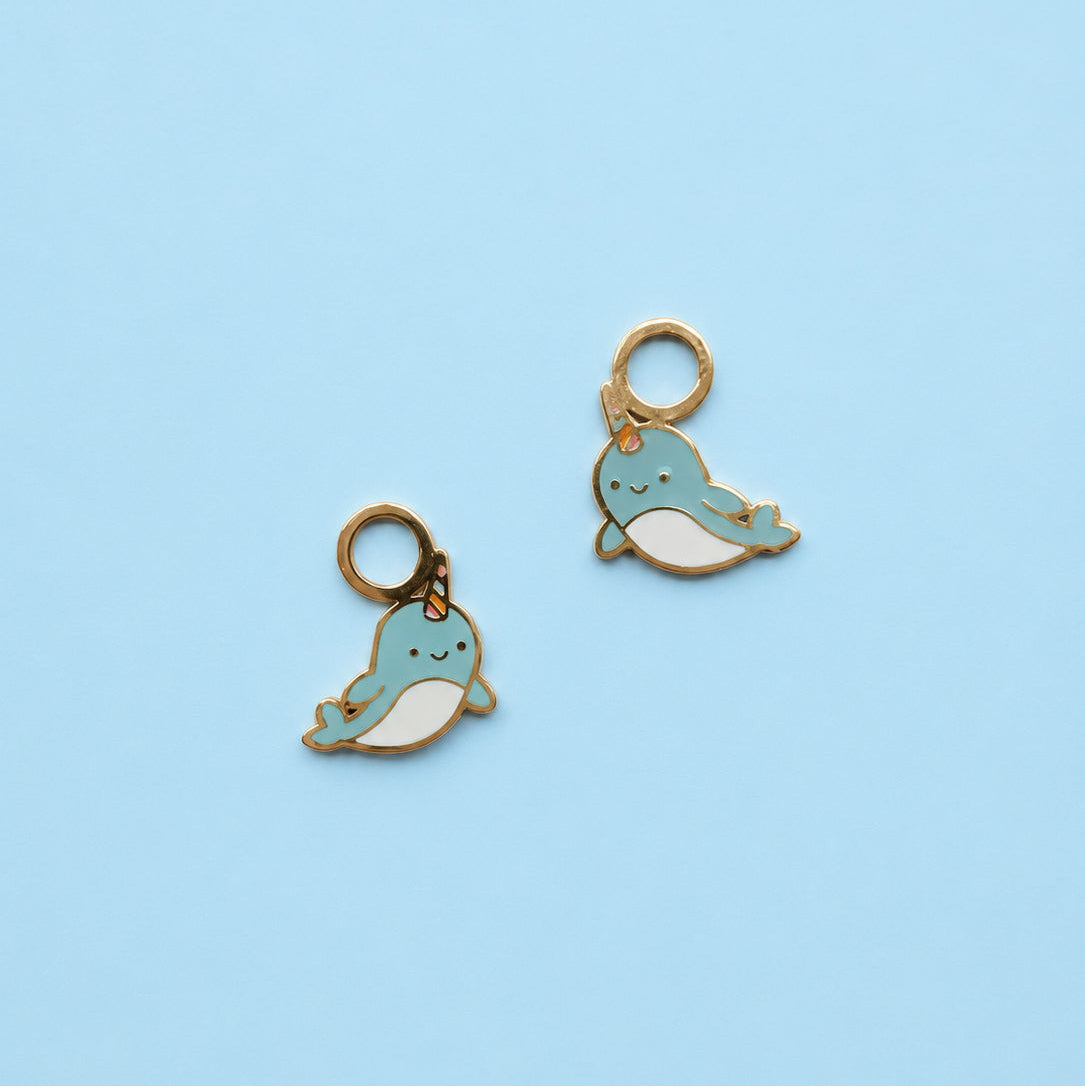 Two blue narwhal-shaped charms on a light blue background