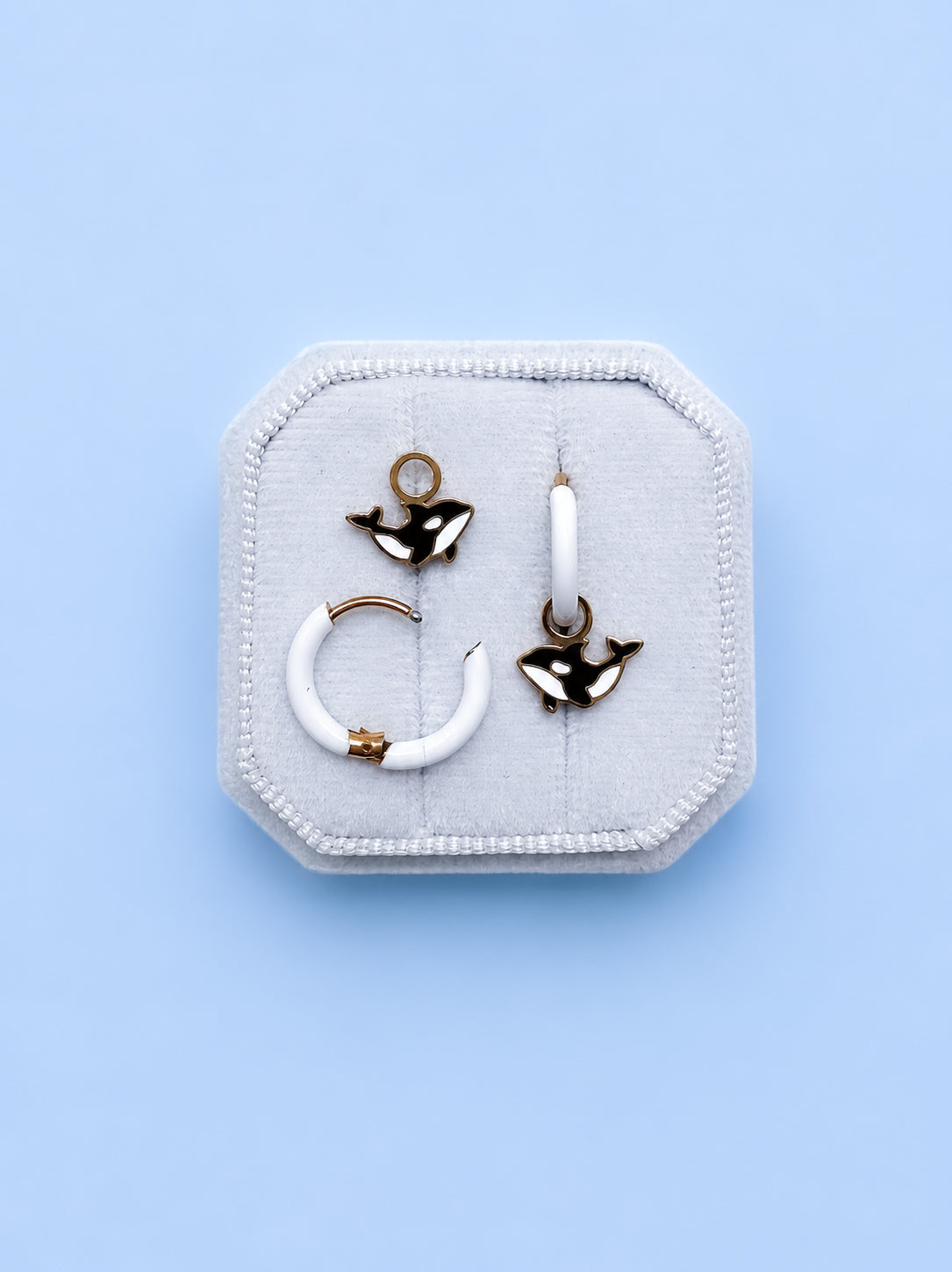 Jewelry set with black and white orca whale charms with white huggie hoop earrings on a light blue background