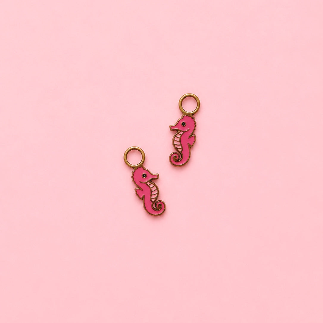 Two pink seahorse-shaped charms on a pink background