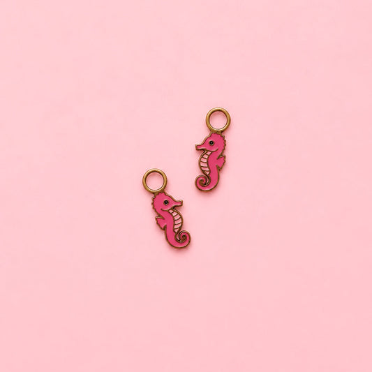 Two pink seahorse-shaped charms on a pink background