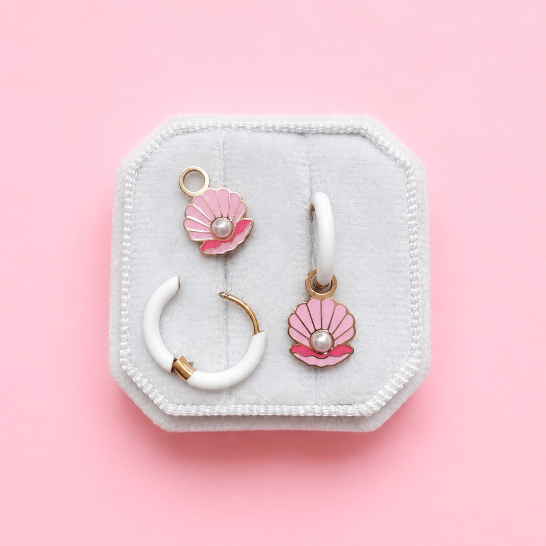 Jewelry set with pink seashell charms with pearl details on a white jewelry box on a pink background