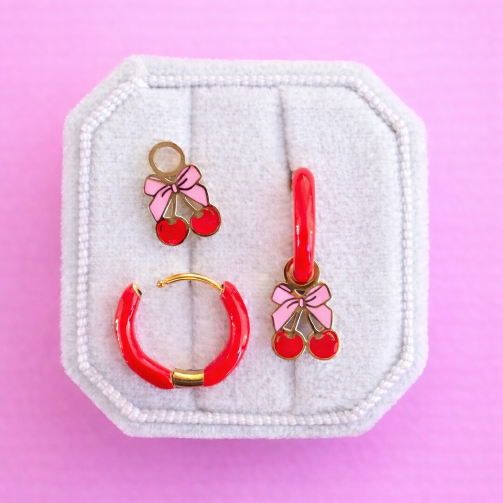 Pink bow cherry charms on red huggie hoops on a white jewelry box on  a pink background