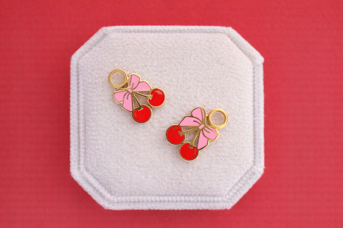 Pink bow cherry charms on a white jewelry box on a red background