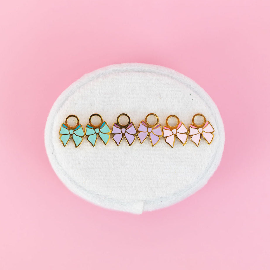 Set of mint, lavender, and light pink bow-shaped charms on a white round cushion against a pink background
