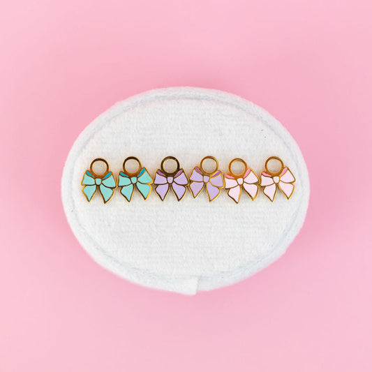 Set of colorful bow-shaped earrings on a white round cushion against a pink background