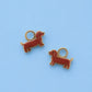 Two small dachshund-shaped jewelry charms with gold-tone metal outlines and loops, shown on a light blue background.