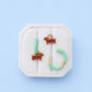 A set of  earrings displayed on a white fabric jewelry stand against a light blue background. The set includes two small brown dachshund dog charms, a mint green bar, and a matching mint green hoop with gold ear wires.