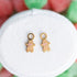 Gingerbread huggie charms on a white jewelry cushion against a red and green background