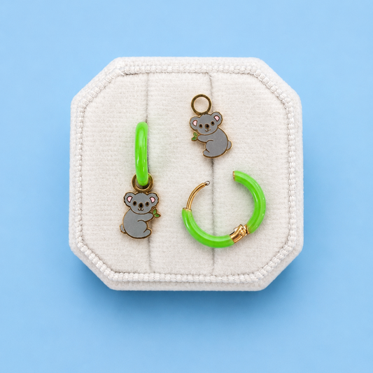 Koala huggie charms on green huggie hoops on white jewelry box with blue background