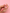 A hand with pink manicured nails holds a small enamel charm shaped like a pink milk carton with a strawberry and a white loop at the top, set against a solid pink background.