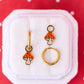Mushroom-shaped earrings on a white jewelry cushion with a red background