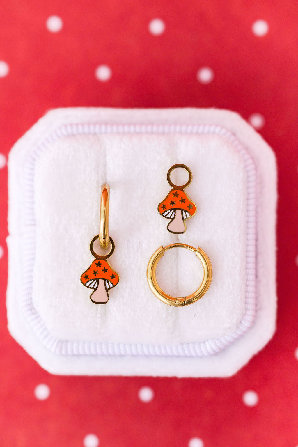 Mushroom-shaped earrings on a white jewelry cushion with a red background