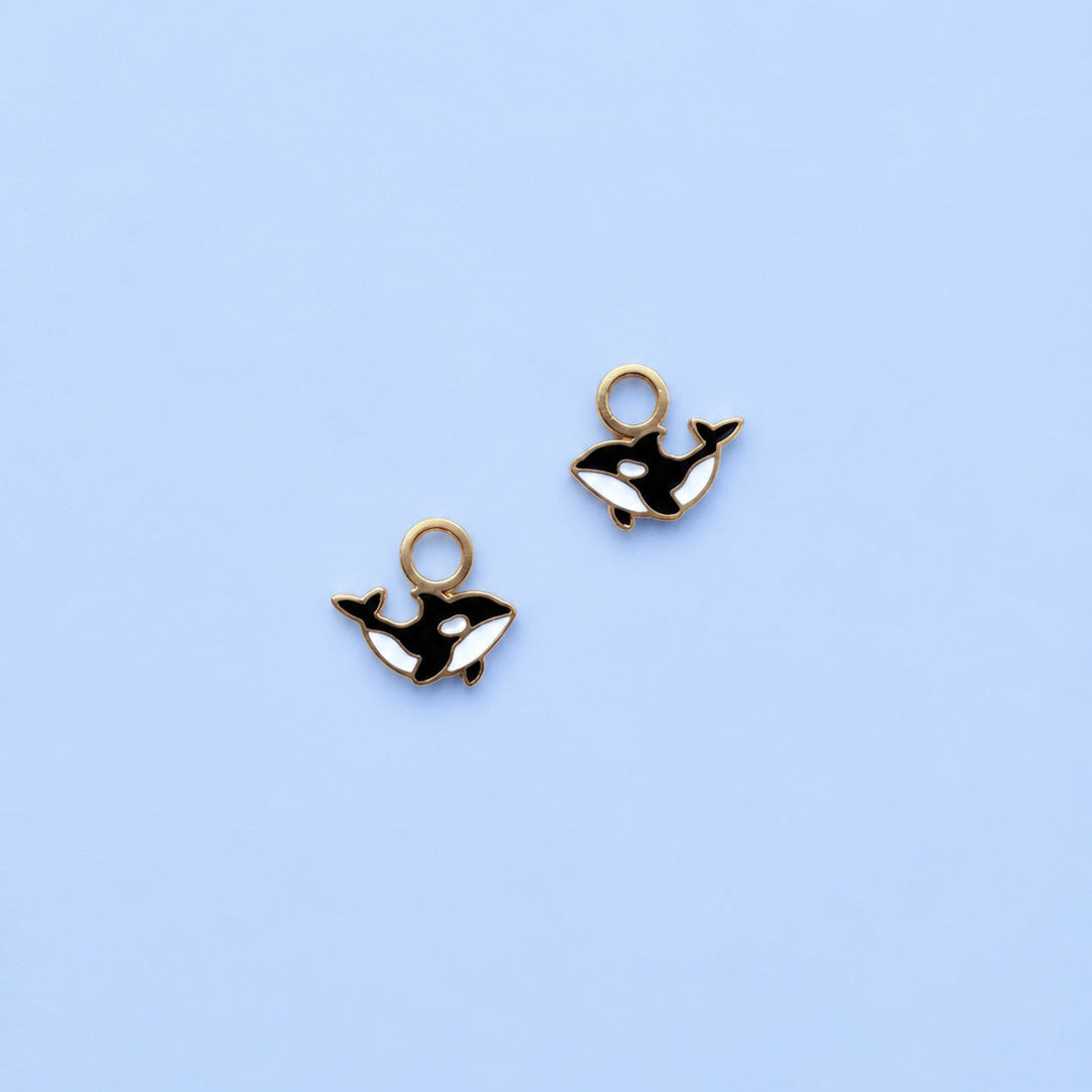 Two gold whale-shaped charms on a light blue background