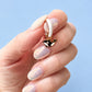 Hand holding a small earring with a whale design against a light blue background