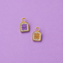 Two small enamel charms shaped like toast slices with cute faces, one purple and one tan, on a solid lavender background.