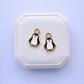 Penguin-shaped earrings on a white jewelry box with a light purple background